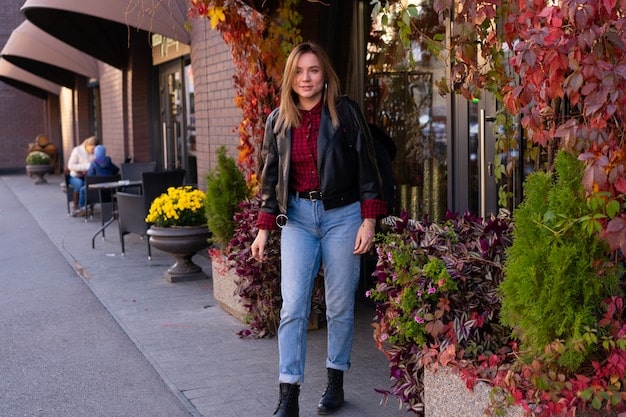 A stylish woman wearing a casual chic outfit, consisting of a blazer, jeans, and ankle boots, walking down a city street with confidence and a blurred background of cafes and shops.