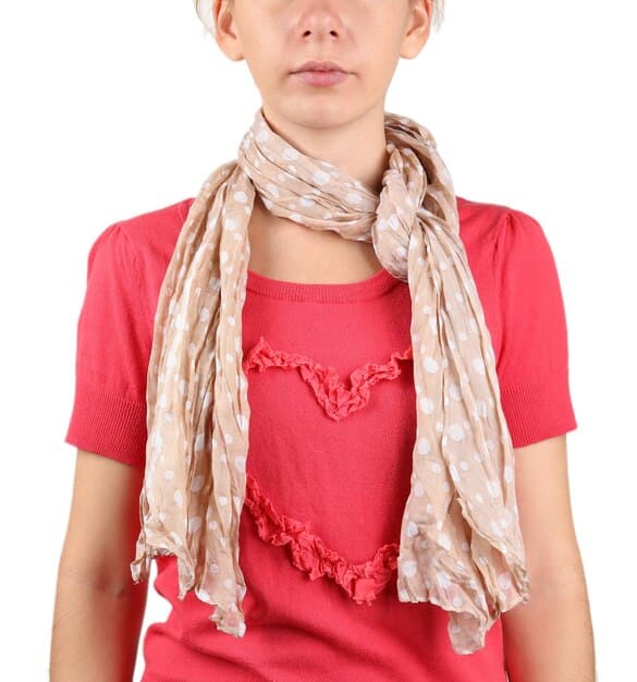 A woman demonstrating different ways to style a scarf, including tying it around her neck, wearing it as a headscarf, and draping it over her shoulders. The lighting is natural and highlights the fabric's texture.