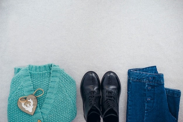 A flat lay of casual clothing items: a pair of jeans, a t-shirt, a sweater, sneakers, and a baseball cap. The items are neatly arranged on a light-colored surface, showcasing a relaxed and comfortable style.