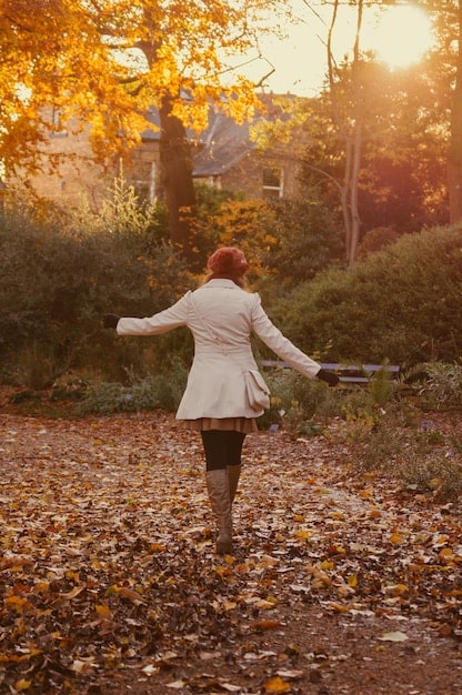 A person walking in a park, focusing on the leaves changing colors in autumn. The image captures the details of the leaves and the sunlight filtering through the trees, emphasizing the beauty of nature.