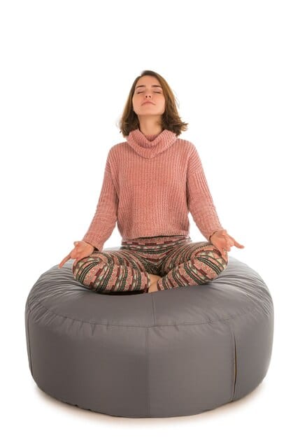 A person sitting cross-legged on a meditation cushion, eyes closed, with a peaceful expression. The background is softly blurred, depicting a serene room with natural light and minimal distractions, symbolizing the ideal environment for practicing mindful listening.