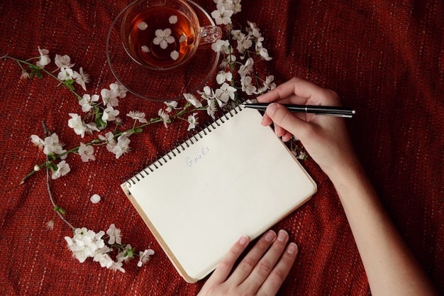 A close-up of a hand writing affirmations in a journal with a pen. The journal is open on a wooden desk, with a cup of tea and a small potted plant nearby, creating a peaceful and reflective atmosphere.