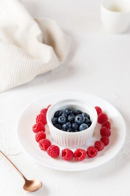 A close-up shot of fresh blueberries in a small bowl on a kitchen counter. The focus is on the vibrant blue color and the natural texture of the berries. Sunlight streams in from a nearby window, enhancing the visual appeal.