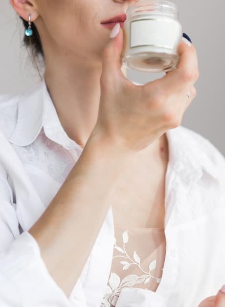 A woman applying lotion to her wrist, with a bottle of perfume visible in the background. The image highlights the importance of moisturizing before applying fragrance.