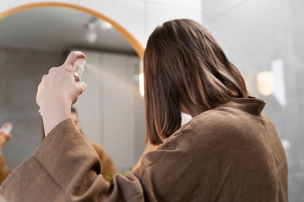 A person's hands gently applying perfume to their hair, with the fragrance mist visibly suspended in the air before settling on the hair strands. The background is a well lit space that helps to isolate the main action.