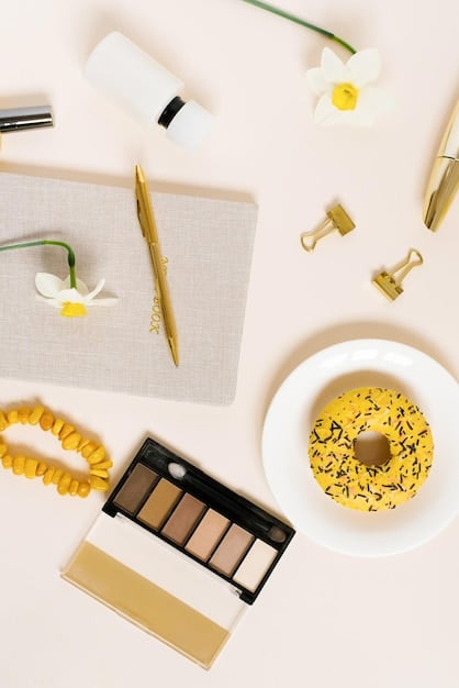 A flat lay of high-quality makeup products arranged around a small, open eyeshadow palette featuring smoky shades. Products include a primer, mascara, blending brush, and a setting spray, all beautifully lit.