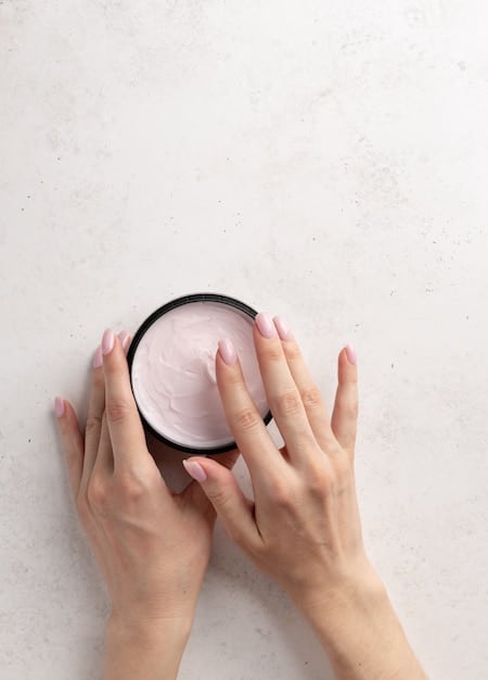 A woman's hand demonstrating the application of cream blush to her cheek with fingertips, showing a soft, blended result on her radiant skin.