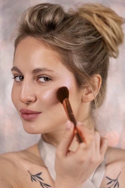 A makeup artist applying a subtle, shimmery cream blush to a model's cheekbones, with natural, healthy-looking skin and light catching the high points of her face, embodying a dewy makeup look.