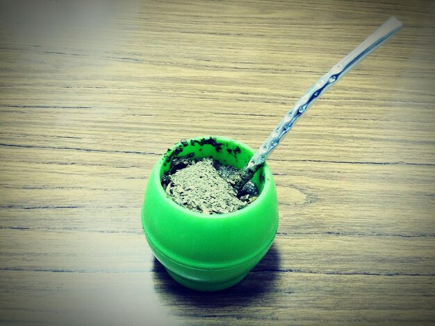 A spoonful of vibrant green spirulina powder being gently sprinkled into a shaker bottle filled with a green smoothie, with a background of gym weights or athletic gear, emphasizing its use in fitness.