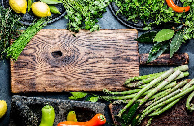 A cutting board with various leafy greens, including watercress, collard greens, and mustard greens, alongside herbs and a knife, depicting the preparation of a diverse meal.