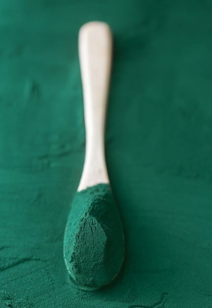A close-up of spirulina powder, dark green and finely textured, with a spoon nearby, suggesting its use as a supplement, against a clean, health-focused background.