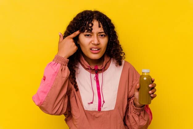 A person holding their head with a pained expression, indicating a headache or fatigue, surrounded by an array of supplements and empty juice bottles, signifying the negative effects of detox diets.