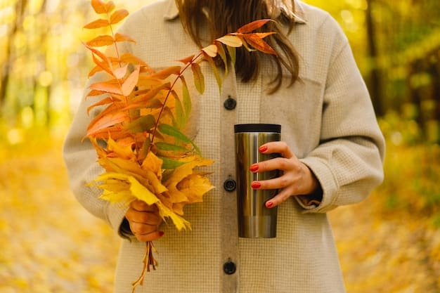 A person's hand reaching for a warm, amber-colored perfume bottle on a wooden table, with sunlight streaming through a window revealing autumn leaves outside.