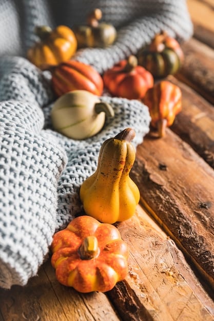 A close-up of an autumn centerpiece with a variety of small, colorful pumpkins, gourds, and dried leaves arranged on a rustic wooden table, with soft, diffused light.