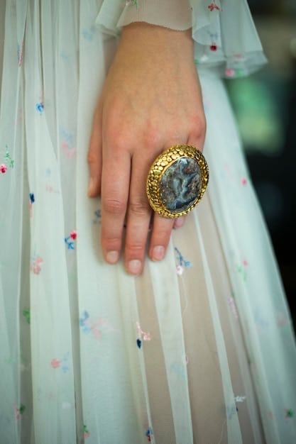 A close-up of a model's hands during Paris Fashion Week SS2025, showcasing an intricately designed, hand-crafted ring with a large, unset gemstone, symbolizing a return to natural and unique jewelry.