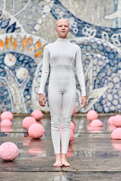 A gender-neutral model wearing an avant-garde, asymmetrical jumpsuit designed by Noah Vance, made from recycled grey technical fabric, in a minimalist, concrete urban setting. The design features sharp lines and modular elements.
