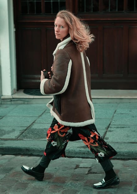 A street style photograph outside a Milan Fashion Week Fall/Winter 2025 show, showing an attendee in a stylish, oversized textured coat with layering, showcasing contemporary outerwear trends.