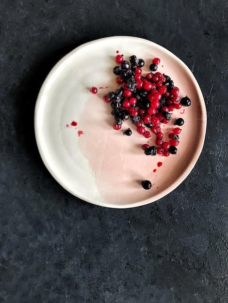 A close-up of a bowl of plain yogurt topped with fresh berries (blueberries and raspberries) and a sprinkle of chia seeds. The yogurt is creamy and inviting, and the berries add a pop of color. The background is a blurred kitchen scene.