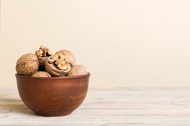 A wooden bowl filled with walnuts in their shells, placed on top of a rustic wooden table. Scattered around the bowl are a few shelled walnuts, revealing their textured surface and golden-brown color. The lighting is warm and inviting, highlighting the natural appeal of the walnuts.