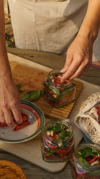 Close-up shot of hands preparing a salad in a mason jar, layering ingredients like dressing, grains, vegetables, and protein. The image is focused on the process of layering individual salad components for optimal freshness and portability within the concept of 'Master Meal Prep: Save Time and Eat Healthy All Week Long'.