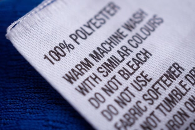 A close-up shot of a garment label indicating that the clothing is made from 100% organic cotton. The label includes certifications from recognized organizations like GOTS (Global Organic Textile Standard). The background is a blurred image of a cotton field being harvested.  The image emphasizes the commitment to sustainable materials used in the wake of reports showing, Is Sustainable Fashion Finally Mainstream? New Data Shows 15% Increase in Eco-Friendly Clothing Sales in US for 2025.