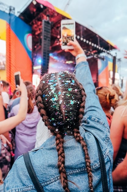 A close-up shot of a person's outfit at a music festival, showcasing a blend of streetwear and bohemian elements. The outfit includes a graphic t-shirt with an artist's name, ripped denim shorts, layered necklaces, and chunky boots, reflecting the diverse styles. The Influence of Music on Fashion is evident in the eclectic mix of textures, patterns, and accessories.