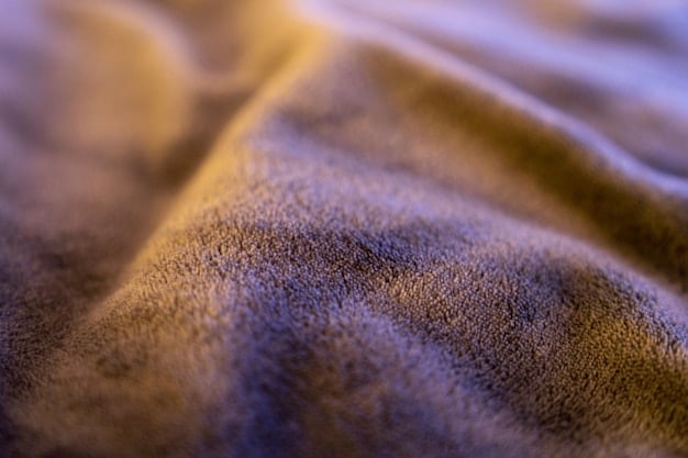 Close-up of a luxurious fabric with intricate, tactile textures, possibly a blend of natural and engineered fibers with a subtle sheen, reflecting the sensorial fabric trend.