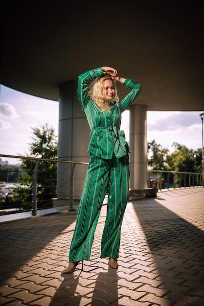 A model wearing a sophisticated olive green utility jumpsuit with fine tailoring and subtle gold hardware, walking down a modern urban street.